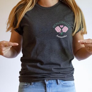 Pu&ograve; includere: T-shirt grigio scuro con un disegno ricamato di racchette da pickleball, un cuore e le parole "Pickleballer" e "Samantha". La maglietta &egrave; realizzata in materiale morbido e ha maniche corte.