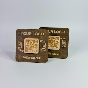 May include: Two wooden QR code signs with the text "YOUR LOGO" and "VIEW MENU". One sign has a tap symbol, the other has a scan symbol. The QR codes are light brown against a dark brown background.