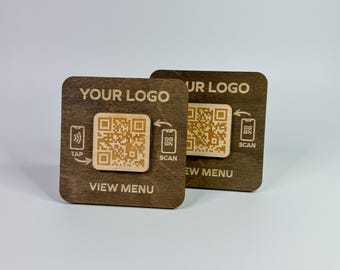 May include: Two wooden QR code signs. Each sign has the text "YOUR LOGO" and "VIEW MENU". One sign has a tap symbol, the other has a scan symbol. The QR codes are light brown against a dark brown background.