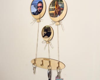 May include: Wooden key holder with three hooks and a sign that says "HOME". The key holder is shaped like a balloon and has three photo frames with pictures of people and a cat.