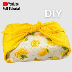 Puede incluir: Envoltorio de tela amarilla atado con un lazo, con un estampado de limones amarillos y blancos. El texto "DIY" y el logotipo de un tutorial de YouTube indican un proyecto de bricolaje.