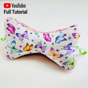 以下が含まれることがあります： 蝶の模様がついた白い枕。枕は骨の形をしていて、両端に緑色のリボンが付いています。