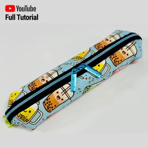 Può includere: Un astuccio per matite blu con chiusura a zip e un motivo di tazze di bubble tea a cartoni animati. Il tiretto della zip ha il testo "Sweet Treat" su di esso.