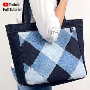 May include: A denim tote bag with a diamond pattern made from different shades of blue denim. The bag has black denim trim and a black handle.