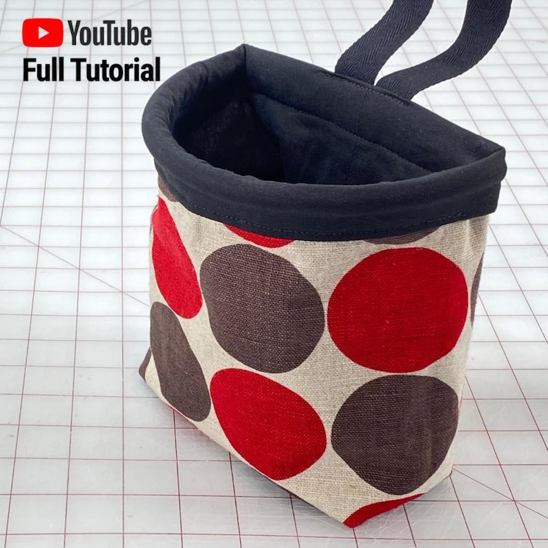 May include: A small, beige fabric bag with a black fabric lining and red and brown polka dots. The bag has a black fabric handle.