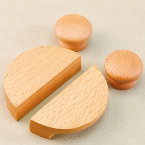 May include: A collection of unfinished wooden cabinet knobs and drawer pulls. The set includes two half-circle drawer pulls and two round knobs, all made of light-colored wood. The items are arranged on a neutral background, showcasing their natural wood grain.