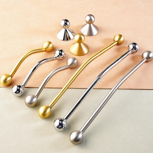 Op de afbeelding: Een verzameling kastbeslag, waaronder goud- en zilverkleurige handgrepen en knoppen. De handgrepen hebben een gebogen ontwerp met kogelvormige uiteinden. De knoppen hebben een afgeronde bovenkant en een conische basis. Neutrale achtergrond.