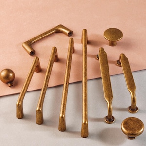 May include: A set of eight antique gold cabinet knobs and pulls. The knobs are round and the pulls are in various shapes, including a curved bar and a straight bar.