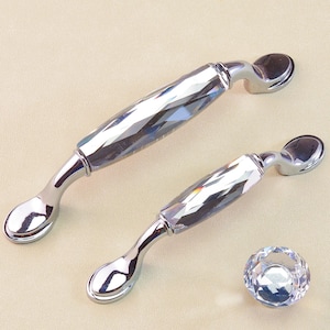 Puede incluir: Dos tiradores de armario plateados y un pomo de cristal. Los tiradores tienen un centro de cristal facetado y un extremo curvo de forma ovalada. El pomo es de cristal facetado con base plateada.