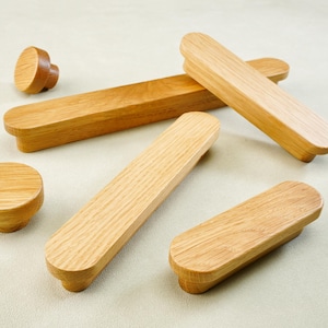 Op de afbeelding: Een verzameling houten kastknoppen en -grepen. De knoppen zijn rond en de grepen rechthoekig met afgeronde uiteinden. Het hout heeft een lichtbruine kleur en zichtbare nerf. Meubelbeslag.