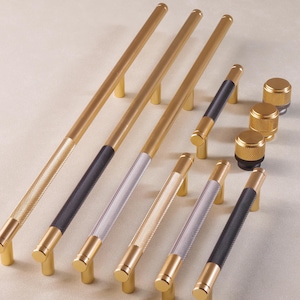 Könnte beinhalten: Ein Satz von acht goldenen, silbernen und schwarzen Schranktürgriffen mit strukturierter Oberfläche. Die Griffe sind in einer Reihe auf einer hellbeigen Oberfläche angeordnet.