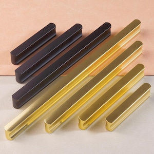 May include: A set of six cabinet pulls in two finishes: black and gold. The pulls are rectangular with rounded edges and a recessed center.