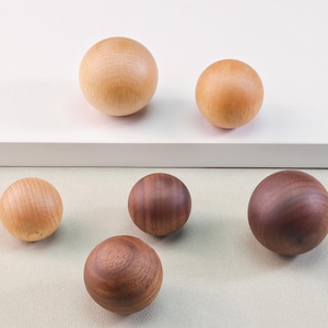 May include: A collection of wooden spheres in varying shades of brown and tan. The spheres are arranged on a white and light green surface, showcasing the natural wood grain and textures. The spheres are of different sizes.