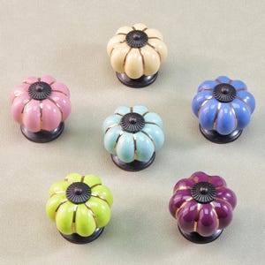 Puede incluir: Seis pomos de cerámica coloridos con forma de flor. Los pomos son en tonos rosa, crema, azul, verde y morado, con detalles dorados y bases negras. Ideales para añadir un toque de color a los muebles.