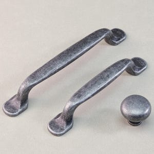 May include: A set of three antique-style cabinet hardware pieces. The set includes two pull handles and one round knob, all with a distressed, weathered finish. The hardware is made of metal and has a gray color.