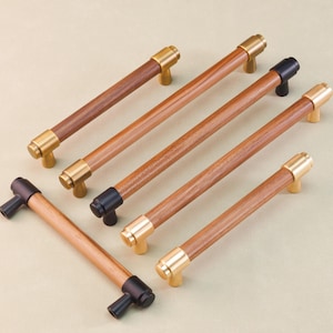 May include: A selection of wooden cabinet pulls with brass and black metal details. The pulls feature a cylindrical wooden body with brass or black metal end caps. The pulls are arranged diagonally on a neutral background.