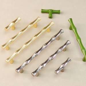May include: A collection of bamboo-style cabinet hardware in gold, silver, and green. The hardware includes various sizes of pulls and knobs, with a natural bamboo stalk design. The hardware is displayed on a neutral background.
