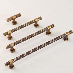 Può includere: Set di ferramenta per mobili color bronzo. Il set include quattro tiranti lunghi e un pomello più piccolo. I tiranti hanno un motivo intrecciato strutturato sulla barra e sulle estremità cilindriche. Per armadi e cassetti.