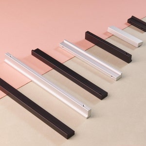 May include: A set of six cabinet pulls in two finishes: black and silver. The pulls are rectangular and have a flat, smooth surface. They are arranged in a row from shortest to longest.