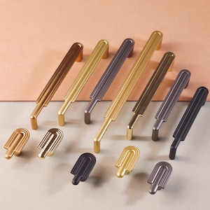 Może przedstawiać: Zestaw ośmiu ozdobnych gałek do szafek w różnych wykończeniach, w tym złoto, mosiądz i czerń. Gałki charakteryzują się unikalnym, geometrycznym wzorem z zaokrąglonymi krawędziami.