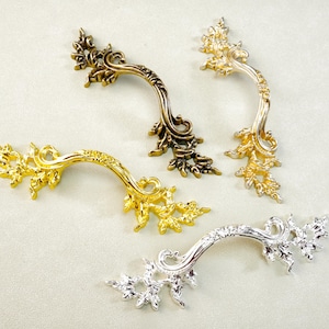 May include: Four decorative cabinet handles in gold, silver, and bronze tones. Each handle features an ornate, curved design with floral and leaf accents, suitable for furniture restoration or DIY projects.