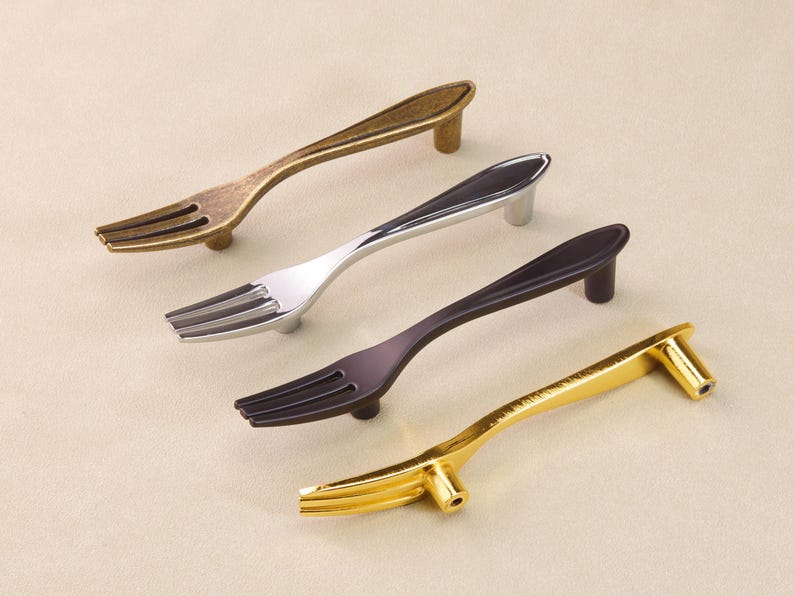 May include: Four cabinet pulls designed as forks, in antique brass, silver, dark bronze, and gold finishes. Each pull has a fork-shaped handle and a small post for mounting. The pulls are designed for use on cabinets and drawers.