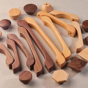 May include: A selection of wooden cabinet hardware, including knobs and pulls, in various shapes and wood tones. The assortment features round knobs, rectangular and hexagonal shapes, and curved pulls, showcasing natural wood grain.