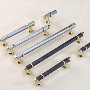 May include: Cabinet hardware set featuring several pull handles and knobs. The handles have a ribbed design in shades of gray and black, with gold-colored accents. The knobs have a similar design. The hardware is designed for cabinets and drawers.