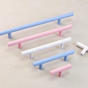 Może przedstawiać: Kolekcja kolorowych uchwytów do szafek w różnych rozmiarach. Uchwyty są w odcieniach niebieskiego, różowego i białego. Okucia są ułożone na jasnej powierzchni, prezentując ich wzór i wariacje kolorystyczne.