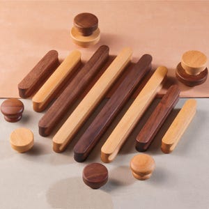 May include: Assortment of wooden cabinet knobs and drawer pulls in light and dark wood tones. The knobs are round and the pulls are long and rectangular.