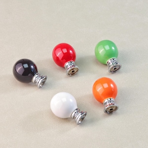 Peut inclure: Cinq boutons de meuble color&eacute;s en noir, rouge, vert, blanc et orange. Chaque bouton a un dessus rond et brillant et une base argent&eacute;e. Ces boutons d&eacute;coratifs conviennent aux meubles ou aux projets de d&eacute;coration int&eacute;rieure.