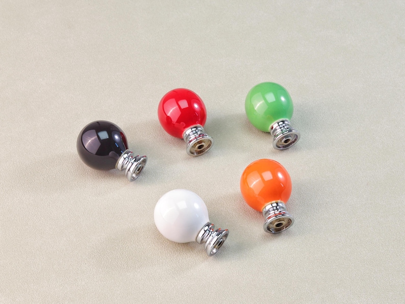Peut inclure: Cinq boutons de meuble color&eacute;s en noir, rouge, vert, blanc et orange. Chaque bouton a un dessus rond et brillant et une base argent&eacute;e. Ces boutons d&eacute;coratifs conviennent aux meubles ou aux projets de d&eacute;coration int&eacute;rieure.