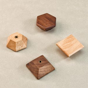 Może przedstawiać: Cztery drewniane kształty geometryczne: sześciokąt, kwadrat i wieloaspektowy kształt, wszystkie w naturalnych odcieniach drewna. Jeden kształt ma mały detal w kształcie gwiazdy. Kształty są ułożone na neutralnym tle.