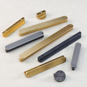 Puede incluir: Una variedad de herrajes para gabinetes modernos en varias formas y acabados. La colección incluye tiradores y pomos dorados, negros y plateados con detalles acanalados. El herraje está diseñado para cajones y armarios.