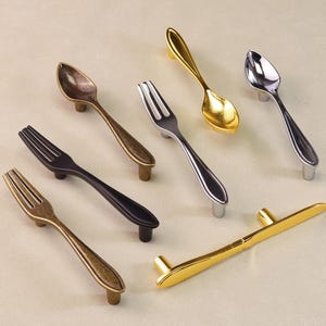 Puede incluir: Una variedad de tiradores decorativos para armarios con forma de cucharas y tenedores. Los tiradores están disponibles en varios acabados metálicos, incluyendo dorado, plateado y bronce. Los tiradores están diseñados para parecer cubiertos.
