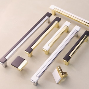 May include: Assortment of cabinet hardware pulls in various styles and finishes. The pulls are made of metal with a polished chrome finish and black or white accents. Some pulls have a gold finish.