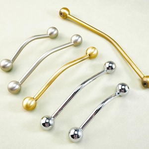 Pode incluir: Uma variedade de puxadores curvos para armários em vários acabamentos metálicos. Os puxadores têm uma extremidade em forma de bola em cada lado e estão em ouro, prata e um acabamento de níquel escovado. O hardware está disposto sobre um fundo claro.