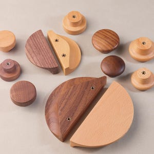May include: Assortment of wooden knobs and pulls in various shapes and sizes. The knobs are round and the pulls are half-circle shaped. Some are made of light wood and others are made of dark wood.