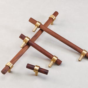 May include: A collection of wooden cabinet pulls with brass accents. The pulls are a rich brown color and feature a cylindrical design with brass rings and posts. The hardware is designed for furniture and cabinetry.