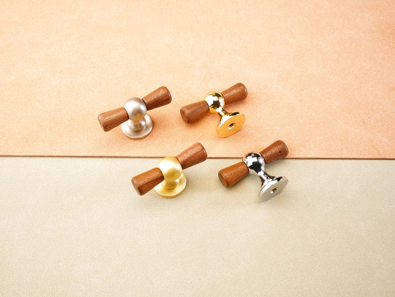 May include: Four cabinet knobs with wooden handles and metal bases. The bases are in silver, gold, and brass tones. The knobs are arranged on a neutral background with a two-tone colour scheme.
