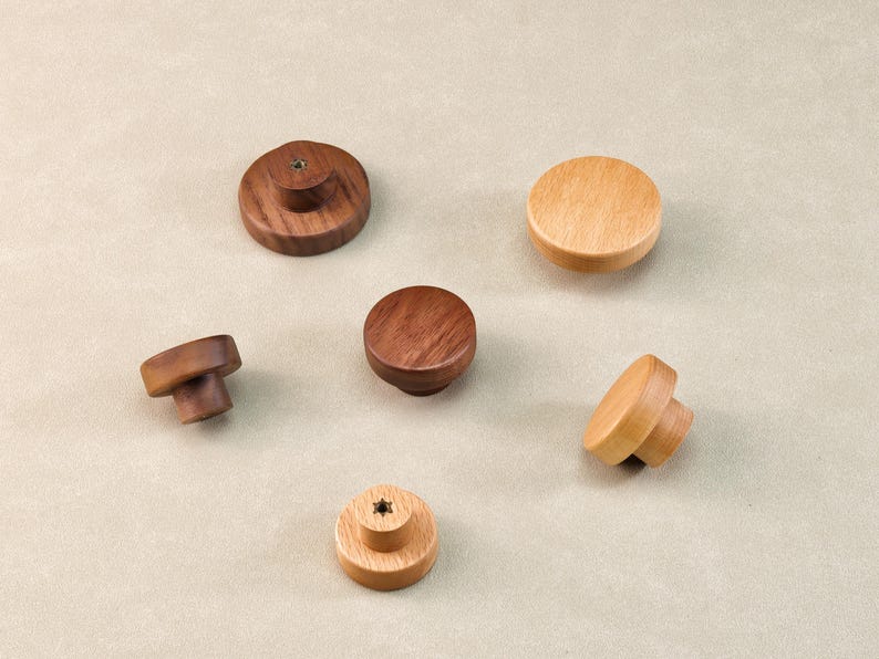 Może przedstawiać: Kolekcja drewnianych gałek do szafek w r&oacute;żnych kształtach i odcieniach drewna. Gałki mają wykończenie z ciemnego orzecha włoskiego, średniego brązu i jasnego klonu. Niekt&oacute;re gałki mają płaską g&oacute;rę, inne zaokrąglony lub grzybkowy kształt.