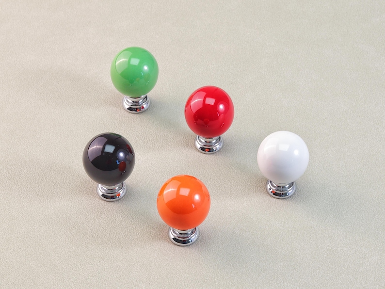 Peut inclure: Cinq boutons de meuble color&eacute;s. Les boutons sont ronds avec une finition brillante, en vert, rouge, noir, orange et blanc. Chaque bouton est mont&eacute; sur une base argent&eacute;e. Les boutons sont probablement destin&eacute;s aux meubles ou &agrave; la d&eacute;coration.