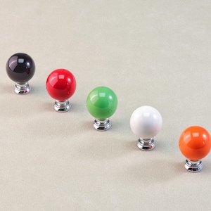Peut inclure: Cinq boutons de meuble color&eacute;s en rang&eacute;e. Les boutons sont ronds avec une finition brillante, en noir, rouge, vert, blanc et orange. Chaque bouton est mont&eacute; sur une base argent&eacute;e.