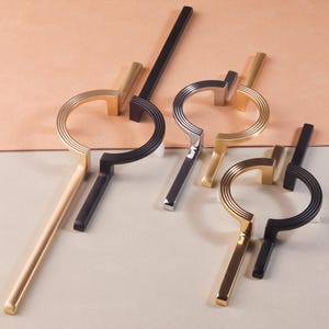 May include: A selection of contemporary cabinet handles in gold, black, and silver finishes. Each handle has a circular grip with linear grooves and a rectangular post. These stylish pulls are designed to enhance the look of furniture, offering a modern touch.