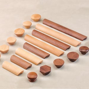 Op de afbeelding: Assortiment van houten kastknoppen en -grepen in verschillende vormen en maten. De knoppen zijn rond, vierkant en zeshoekig. De grepen zijn lang en rechthoekig. Het hout is lichtbruin.