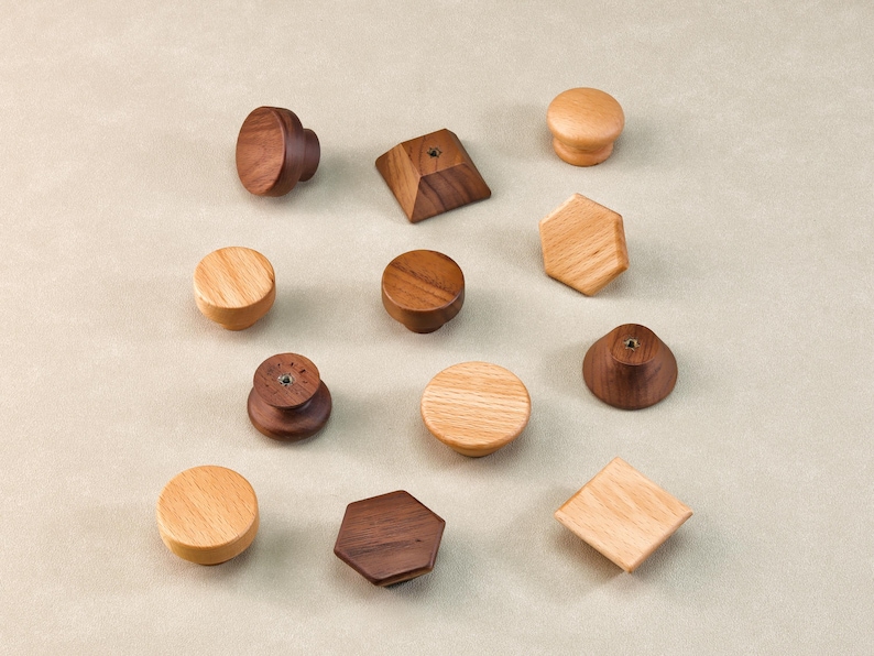 May include: A selection of wooden cabinet knobs in diverse shapes and wood tones. The knobs feature round, geometric, and mushroom-shaped designs, displaying natural wood grain and various finishes. The knobs are arranged on a neutral background.