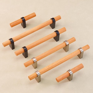 Puede incluir: Un conjunto de tiradores de madera para armarios con acabado natural. Los tiradores tienen mangos cilíndricos de madera y están montados sobre bases de metal oscuro o cepillado. Herrajes para muebles y armarios.