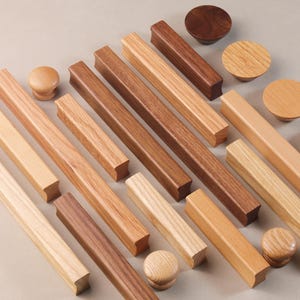 May include: Assortment of wooden cabinet knobs and pulls in various sizes and styles. The knobs and pulls are made of different types of wood, including walnut, maple, and cherry.