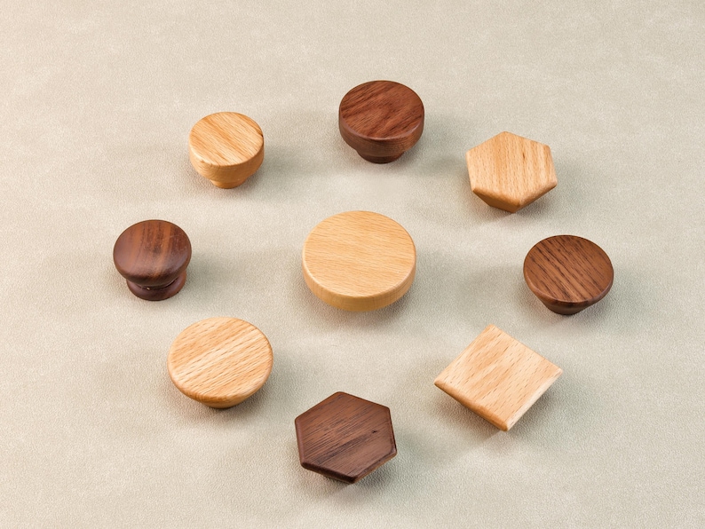 Może przedstawiać: Kolekcja drewnianych gałek do szafek w r&oacute;żnych kształtach i odcieniach drewna. Gałki obejmują okrągłe, sześciokątne i kwadratowe wzory, prezentujące naturalne wzory słoj&oacute;w drewna. Układ podkreśla r&oacute;żnorodność dostępnych styl&oacute;w.