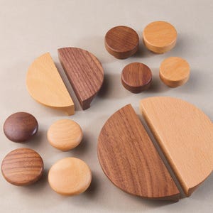 May include: Assortment of wooden cabinet knobs and pulls in two wood tones.  The knobs are round and the pulls are half-circle shapes.